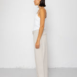 Woman wearing a white sleeveless top and beige pants against a white background