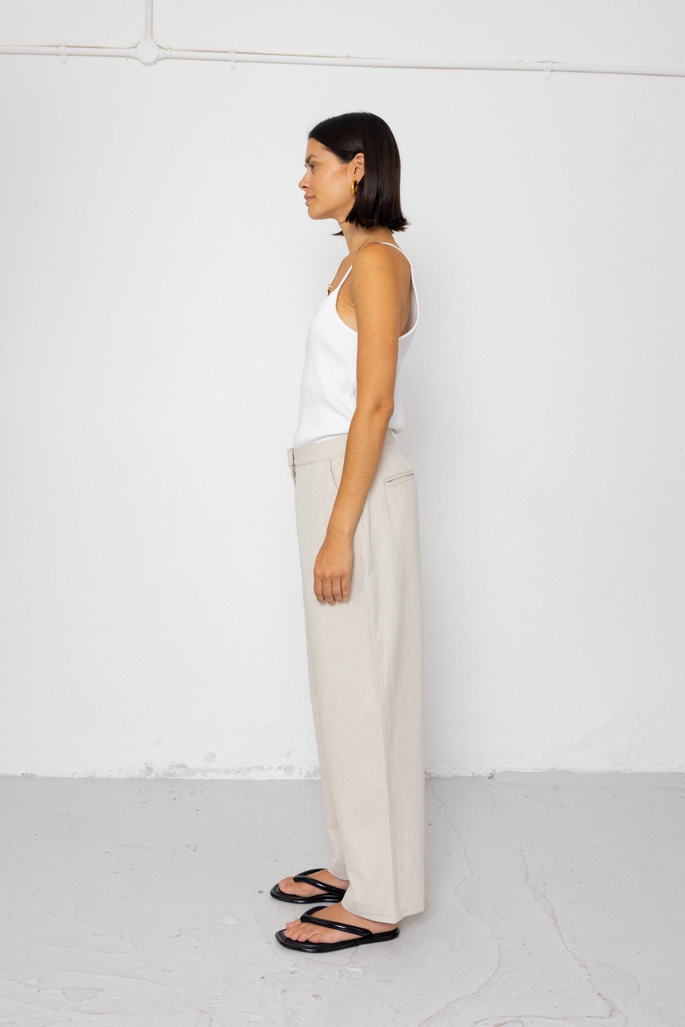 Woman wearing a white sleeveless top and beige pants against a white background