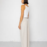 Woman wearing a white sleeveless top and beige pants against a white background