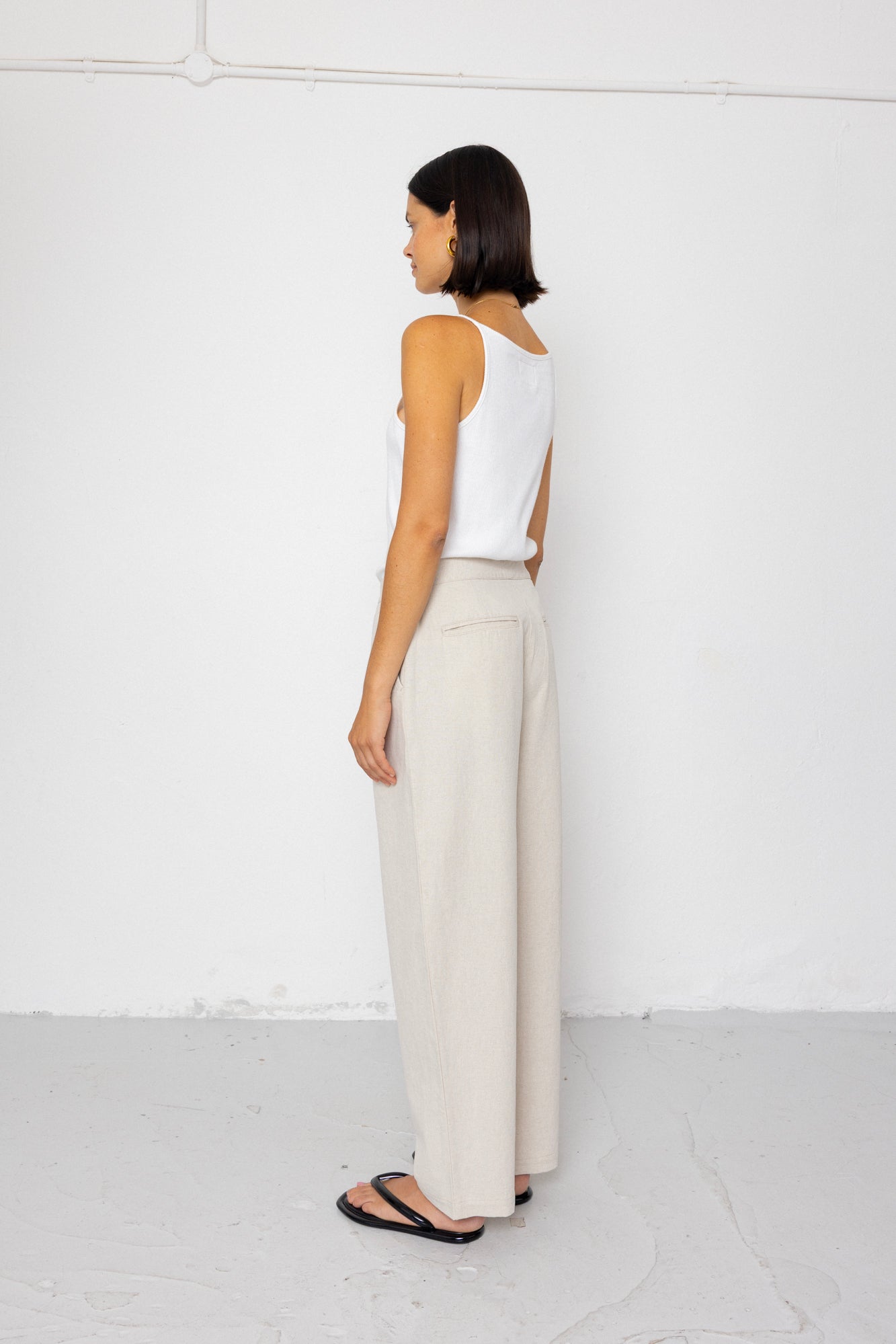 Woman wearing a white sleeveless top and beige pants against a white background