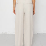 Person wearing beige wide-leg pants and a white top on a white background