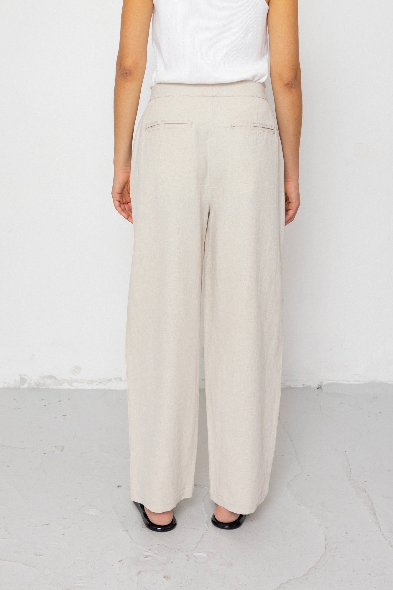Person wearing beige wide-leg pants and a white top on a white background