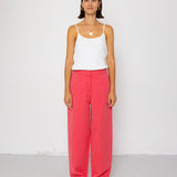 Woman wearing a white tank top and coral pants against a white background