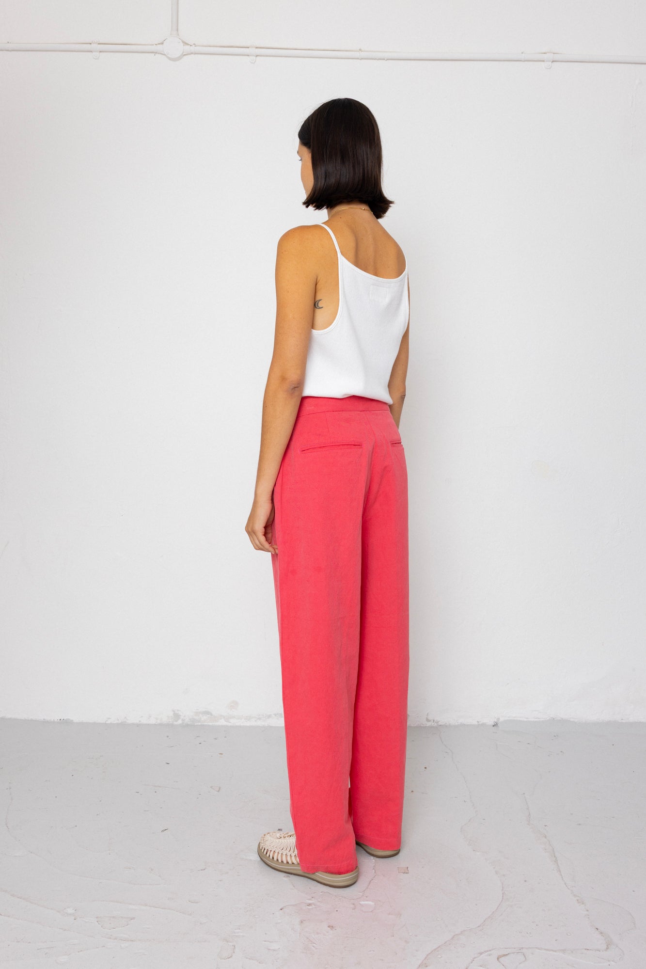 Person wearing a white top and pink pants standing against a white background