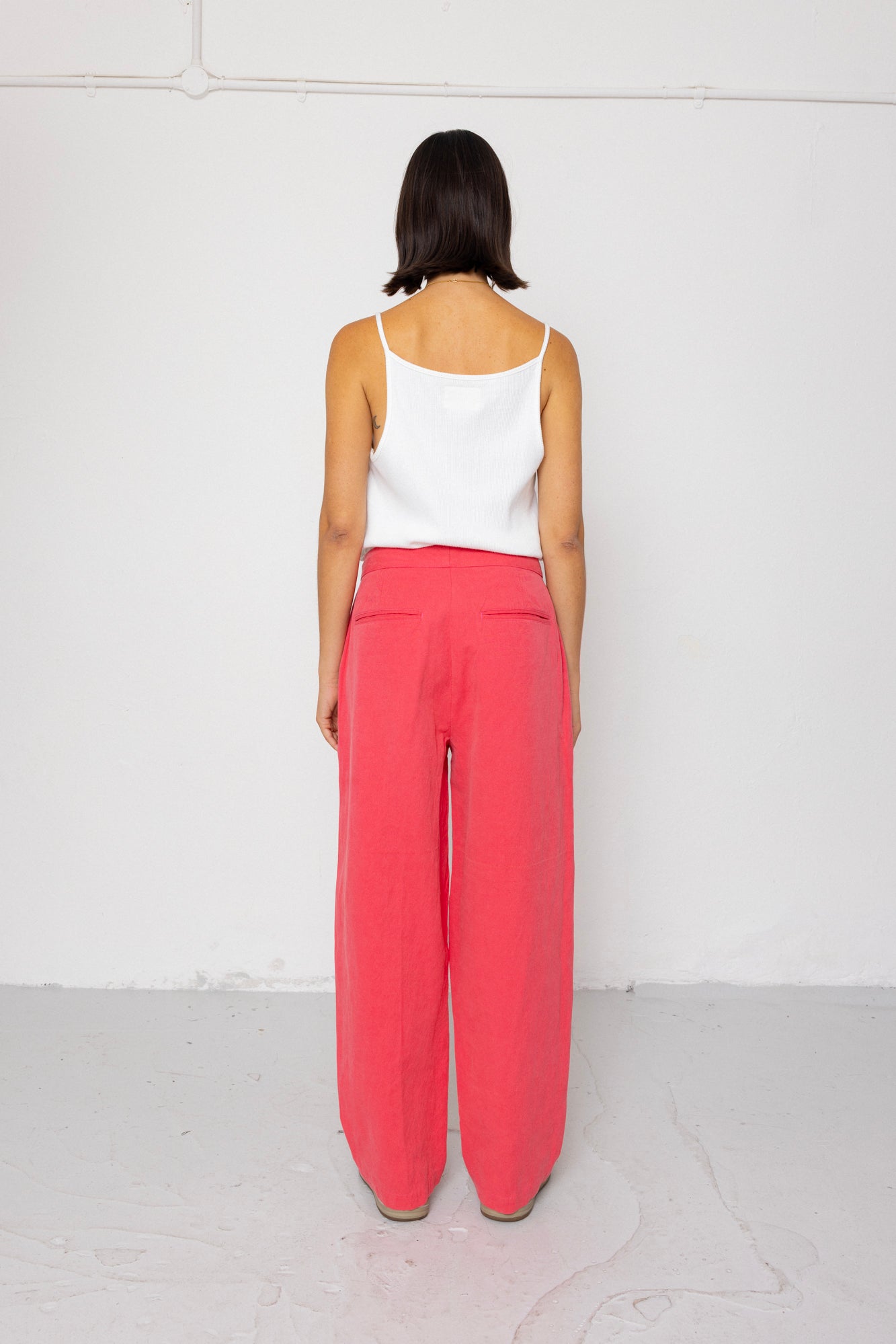 Person wearing a white tank top and coral pants on a white background