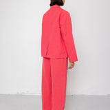 Person wearing a pink suit standing against a white wall.