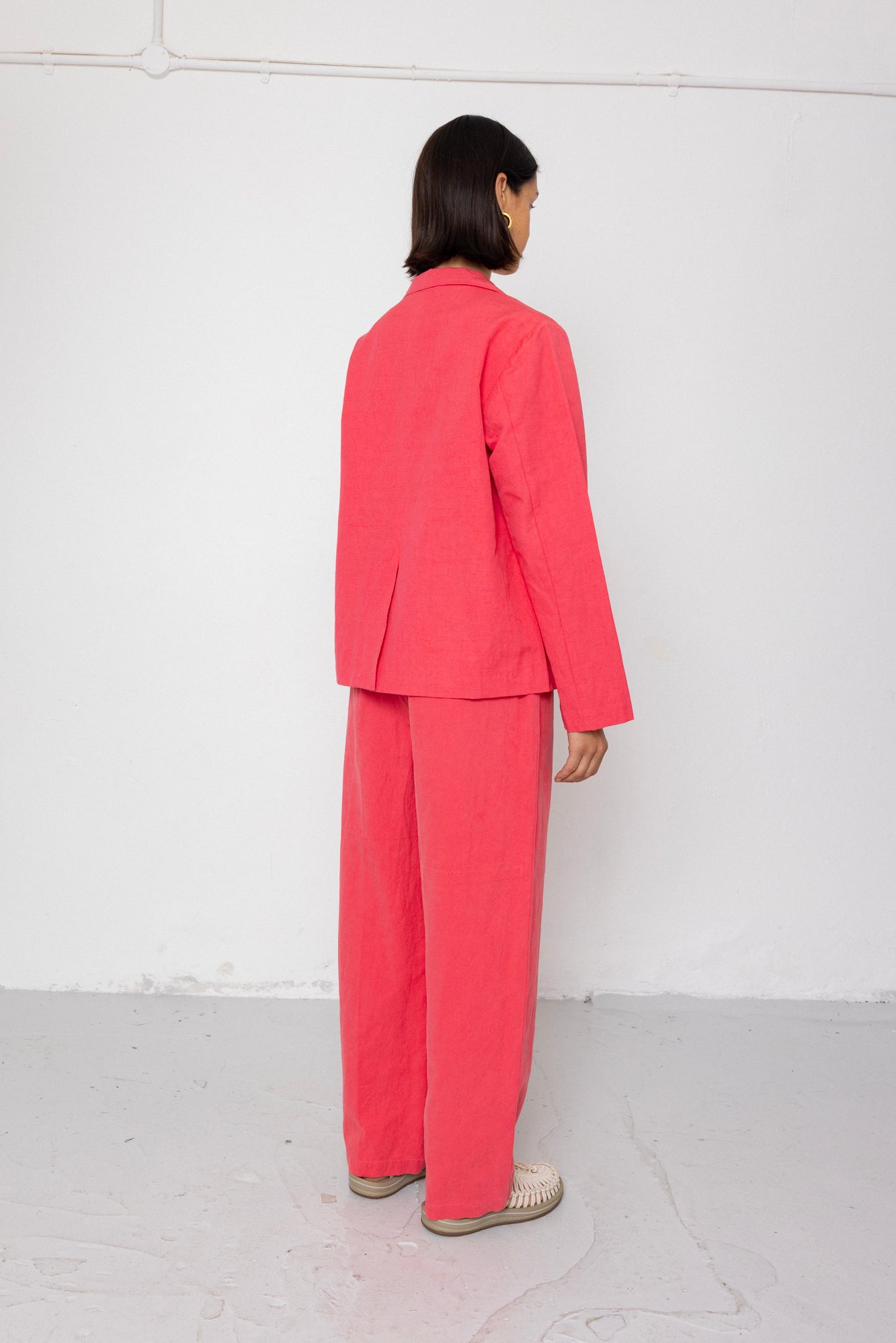 Person wearing a pink suit standing against a white wall.