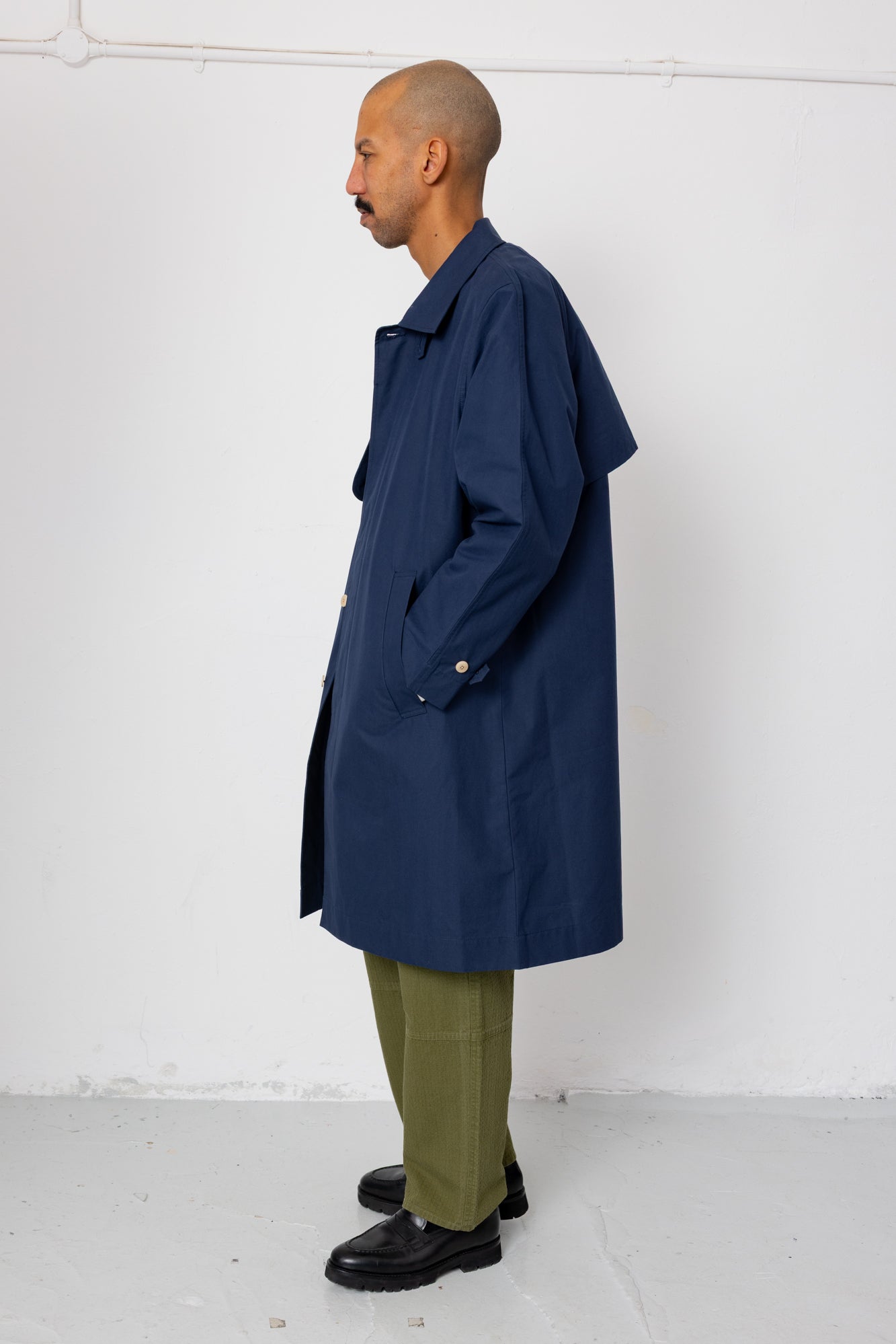 Man wearing a navy trench coat over a green outfit against a white background