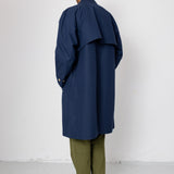 Person wearing a navy blue coat over a green outfit against a white background