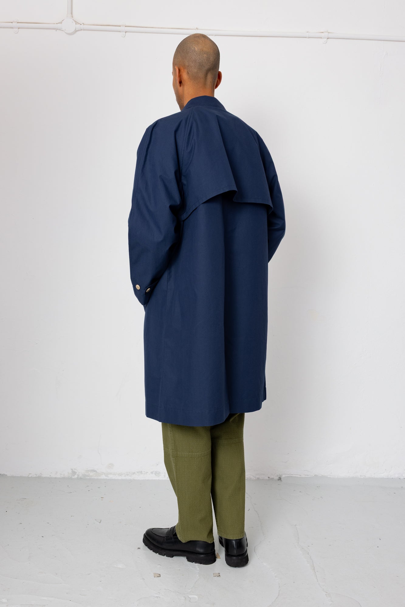Person wearing a navy blue coat over a green outfit against a white background