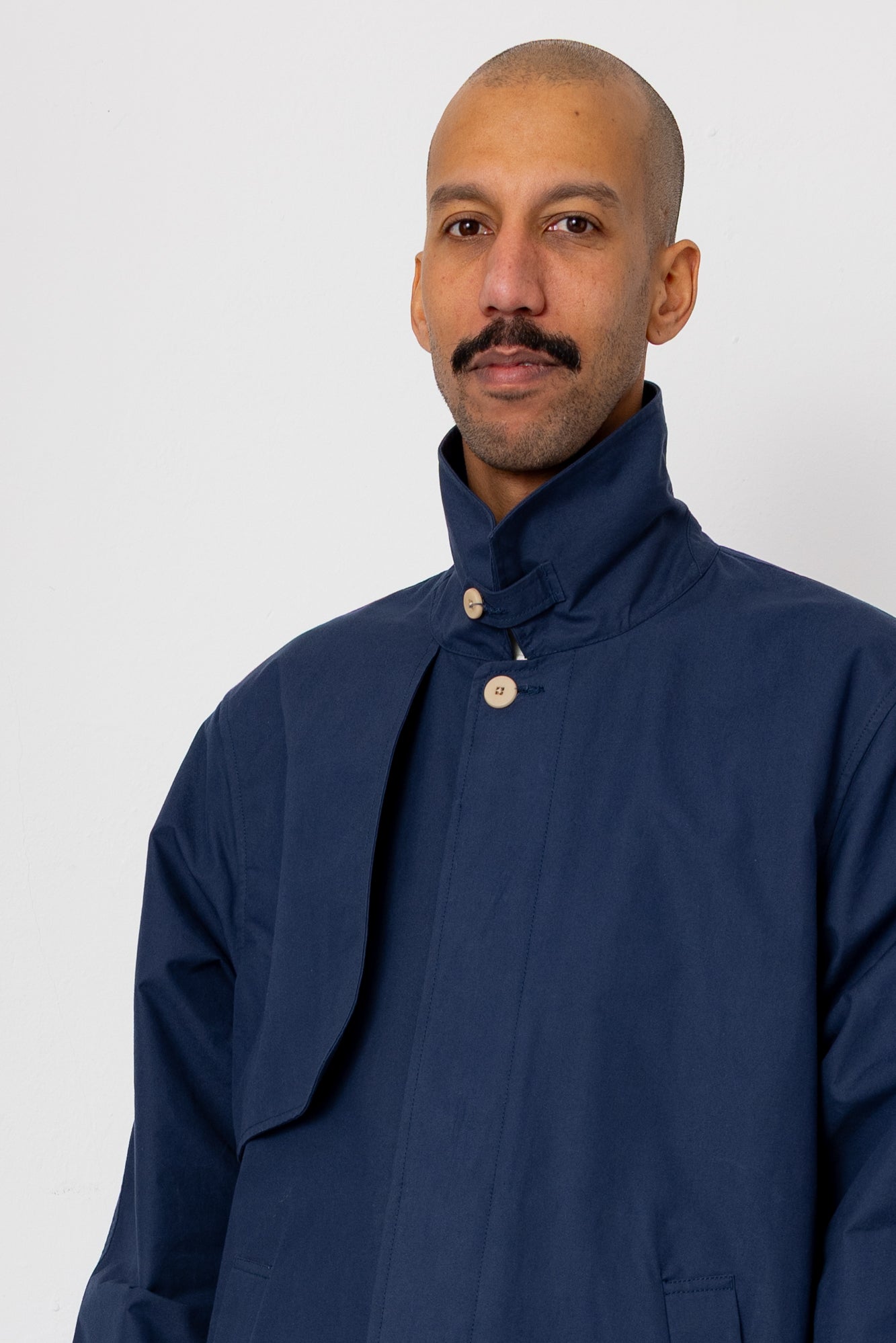 Man wearing a dark blue coat with a high collar on a white background