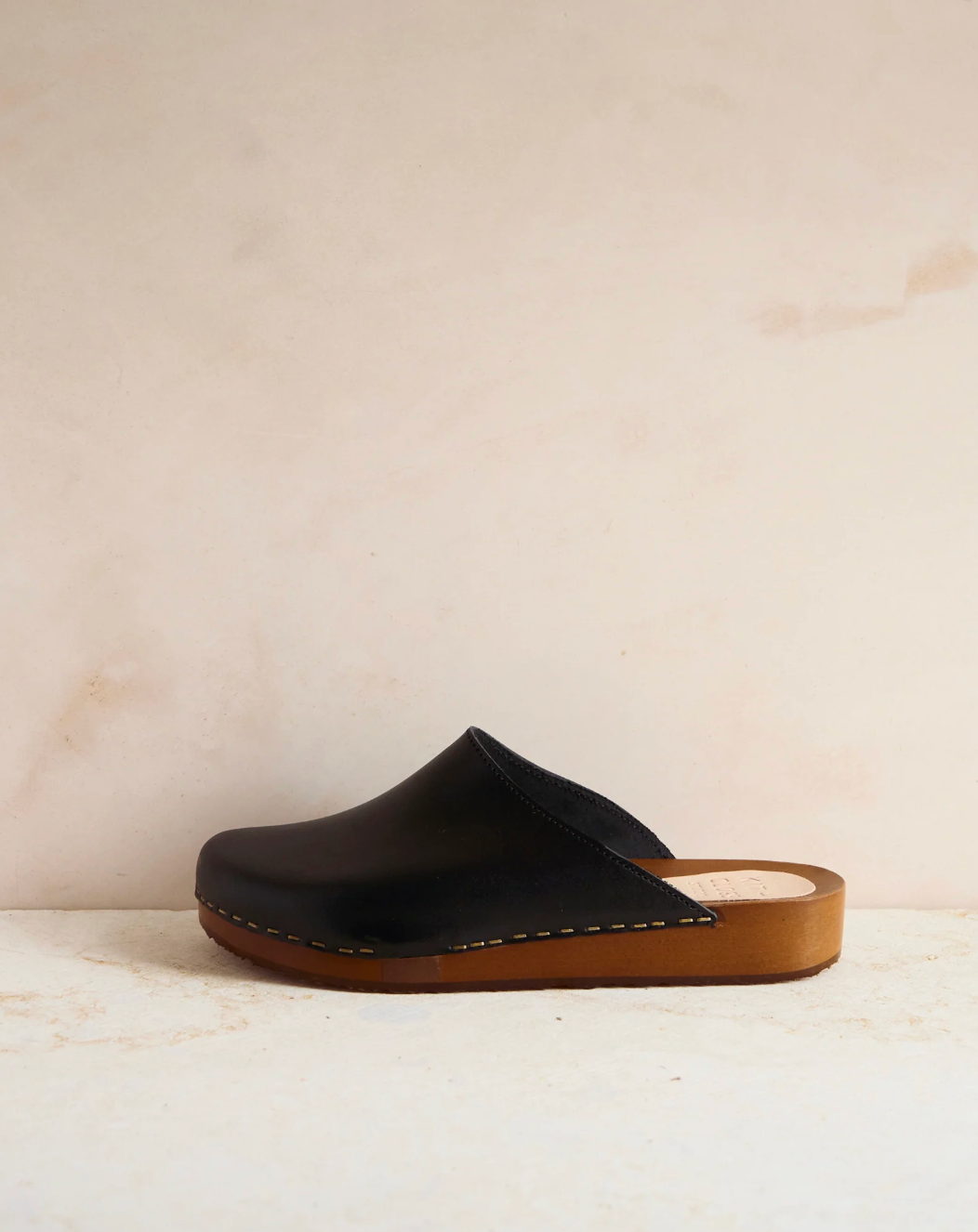 Black clog shoe with brown sole on a beige background