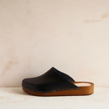 Black clog shoe with brown sole on a beige background