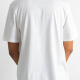 A person shown from the back wearing a plain white short-sleeve crew-neck T-shirt and dark navy pants against a light gray studio background.