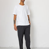 Man wearing a white t-shirt and dark pants against a white background