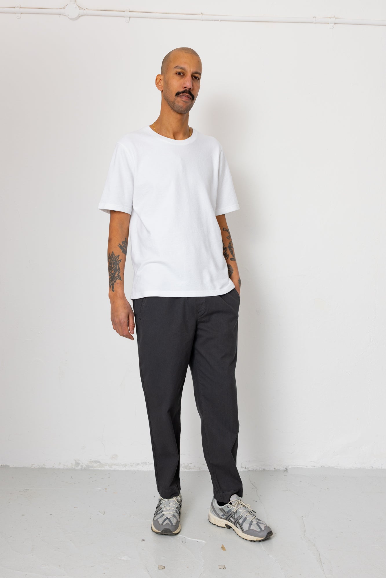 Man wearing a white t-shirt and dark pants against a white background