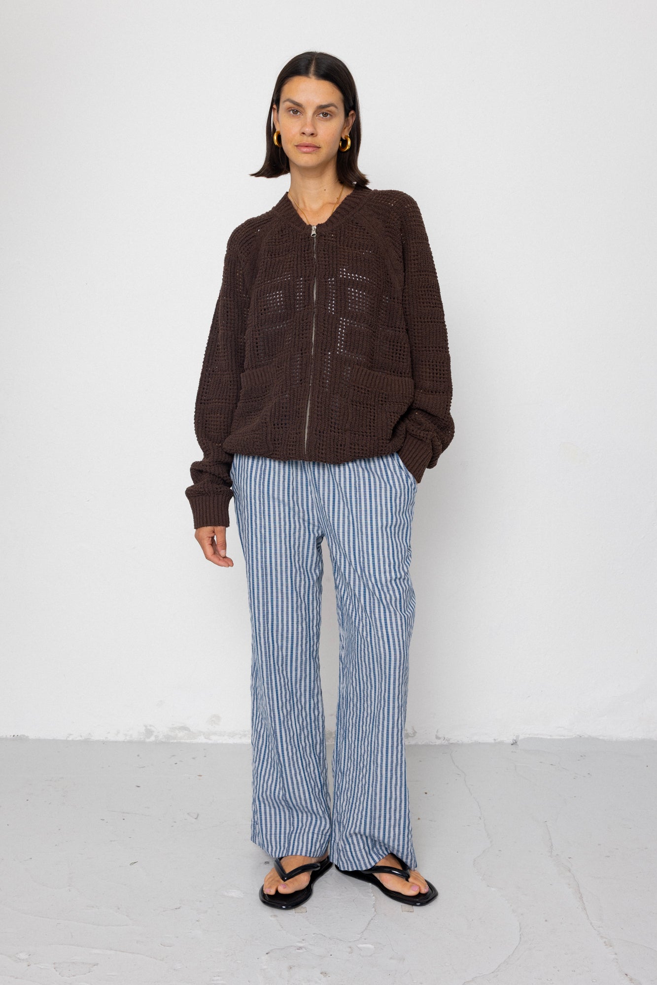 Person wearing a brown jacket and blue striped pants against a white background