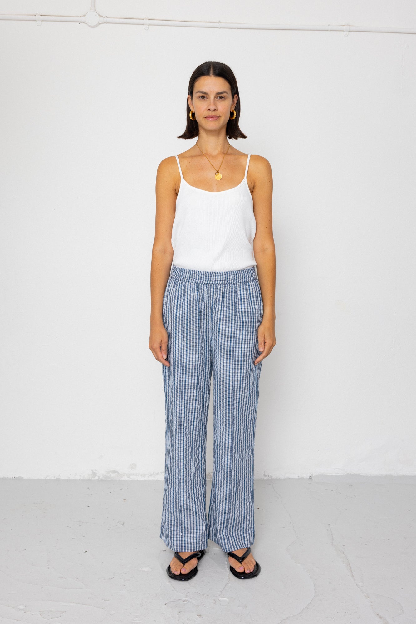 Woman wearing a white tank top and blue striped pants on a white background