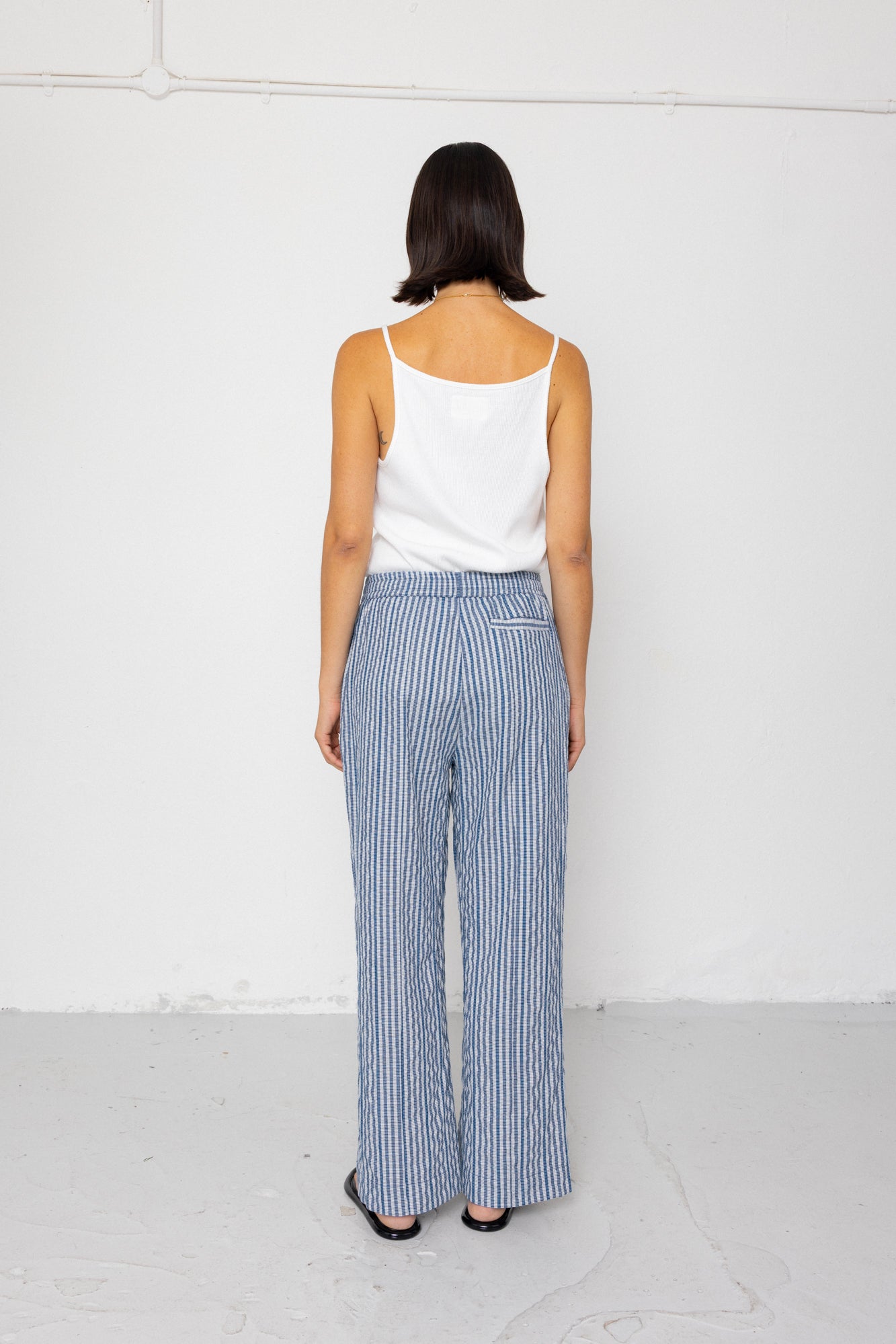 Person wearing a white tank top and blue striped pants against a white background