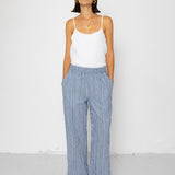 Woman wearing a white tank top and blue striped pants against a white background