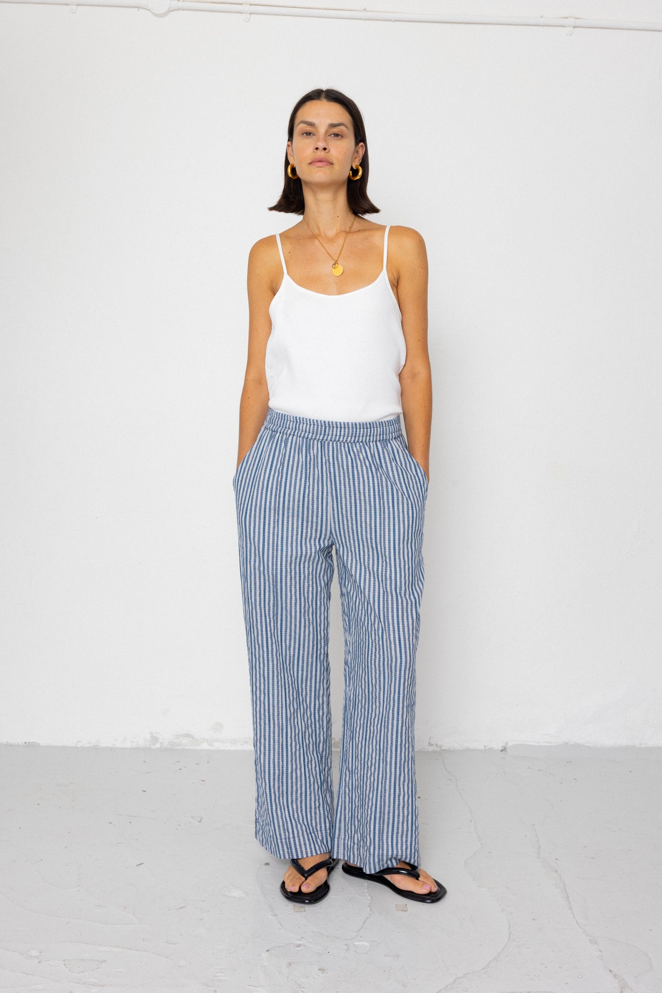 Woman wearing a white tank top and blue striped pants against a white background