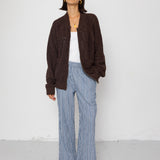 Person wearing a brown jacket, white top, and striped pants against a white background