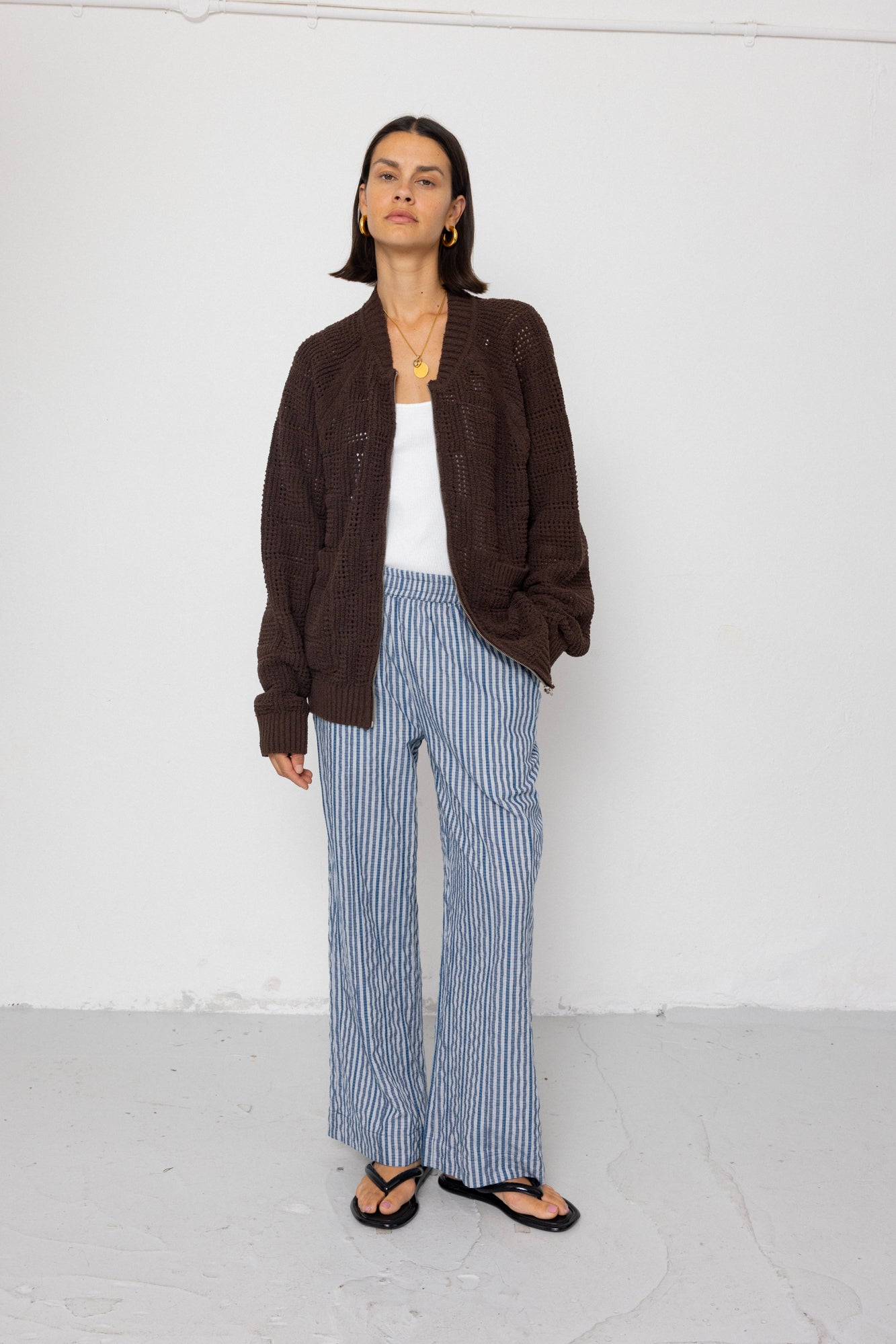 Person wearing a brown jacket, white top, and striped pants against a white background