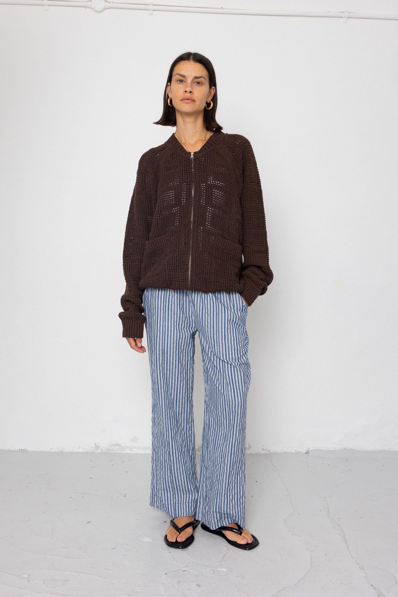 Person wearing a brown jacket and blue striped pants against a white background