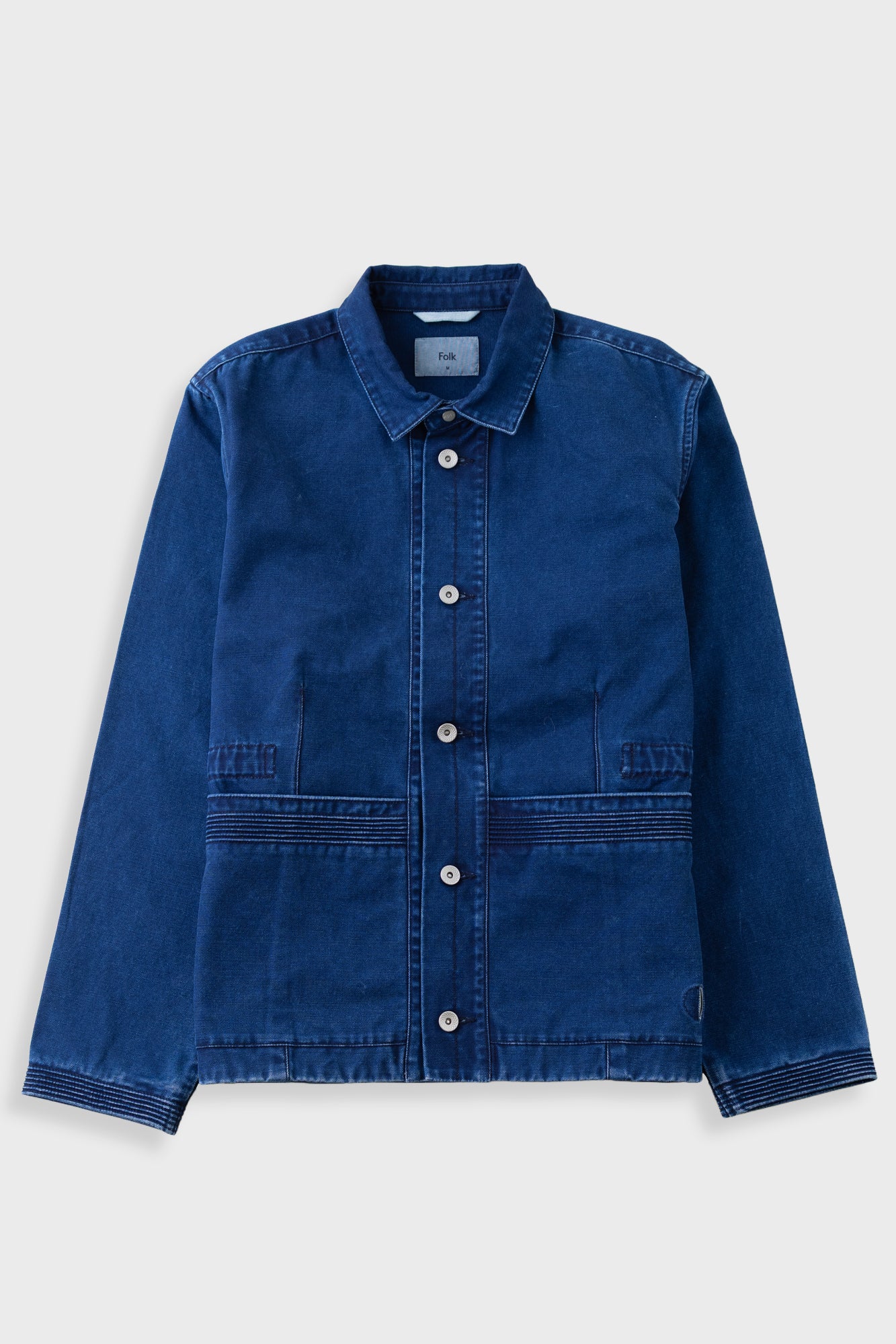 A dark blue denim work jacket with a button-up front, pointed collar, and two front patch pockets, displayed flat against a light gray background.