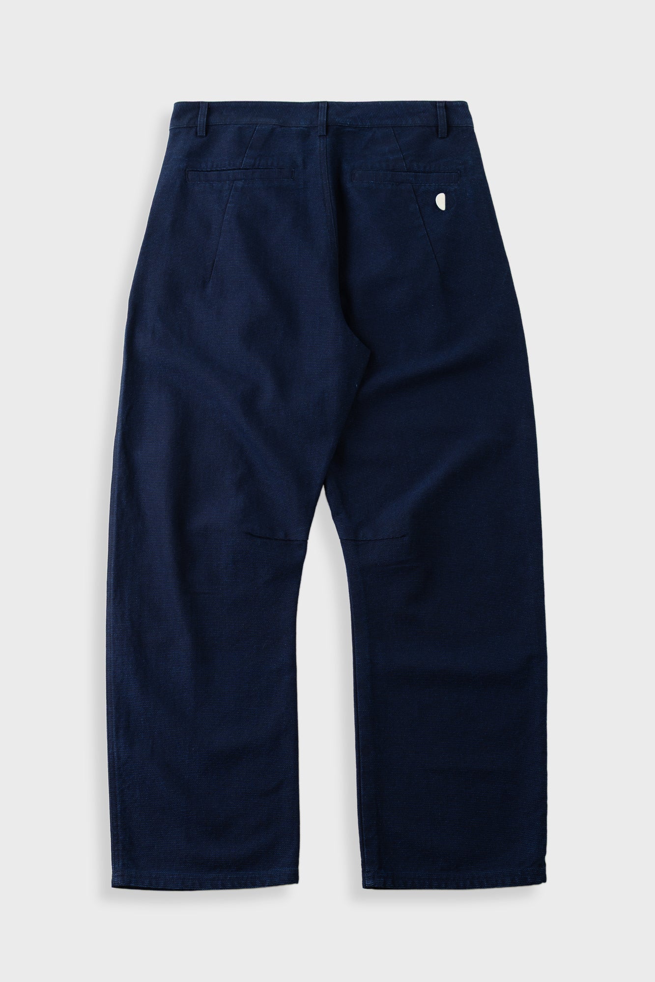 A pair of dark navy blue pants shown from the back, featuring a small white embroidered logo on the upper right side, laid flat against a light gray background.