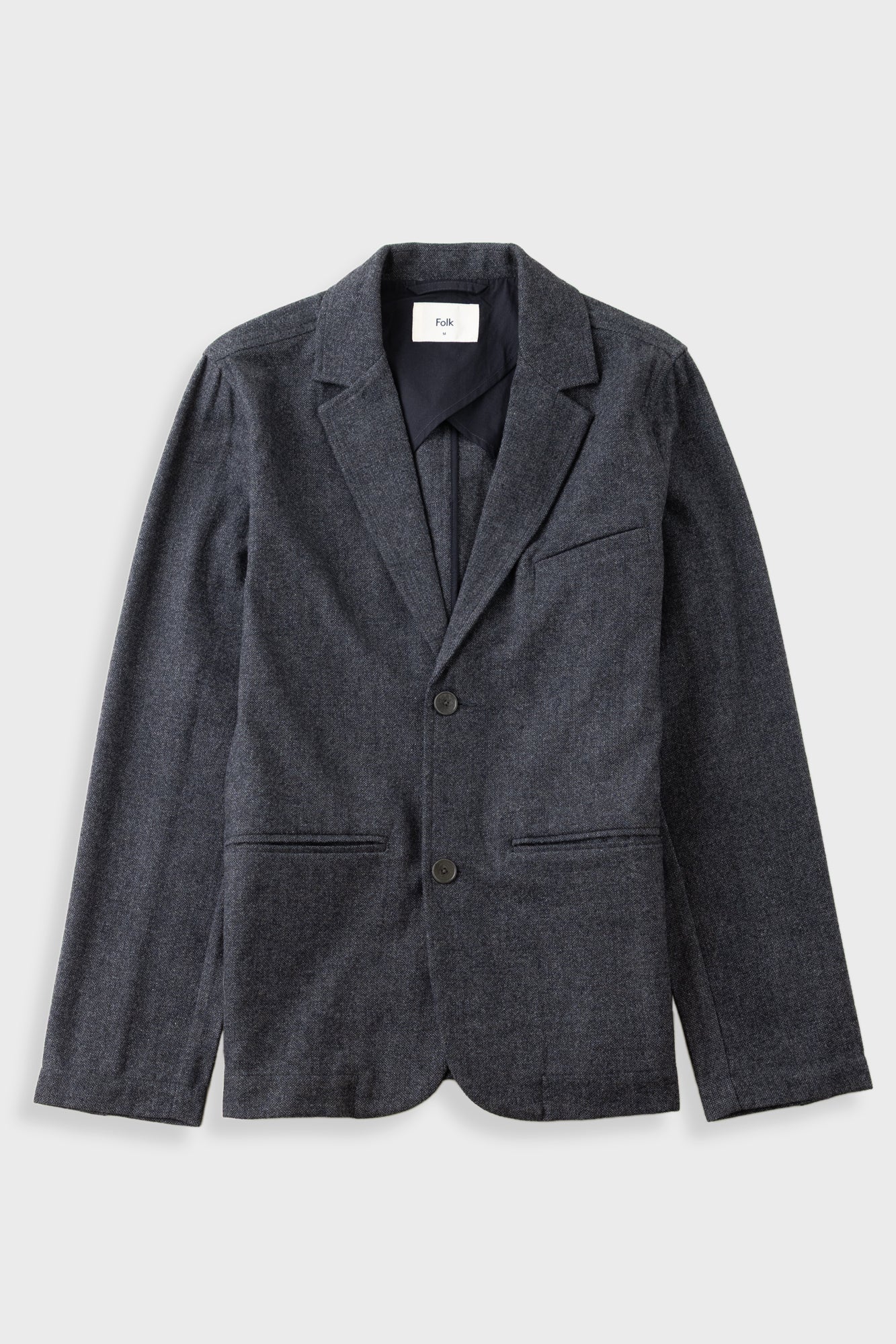 Dark grey blazer laid flat against a light grey background