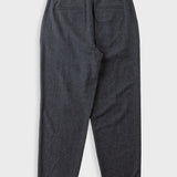 A pair of dark grey pleated trousers laid flat against a solid beige background.