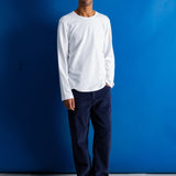 Man wearing navy cord trousers and white t-shirt against a blue background