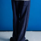 A person shown from the waist down wearing dark navy wide-leg corduroy trousers, a white t-shirt, and black shoes, standing against a vibrant blue wall.