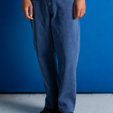 A person wearing loose-fit blue denim pants, a white t-shirt, and black sneakers, standing against a solid blue wall.