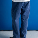 A person shown from the back wearing blue denim jeans, a white t-shirt, and black shoes, standing against a solid blue wall and gray floor.