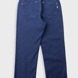 The back view of a pair of dark blue denim jeans, showing the back pockets and button details, photographed flat against a light gray background.