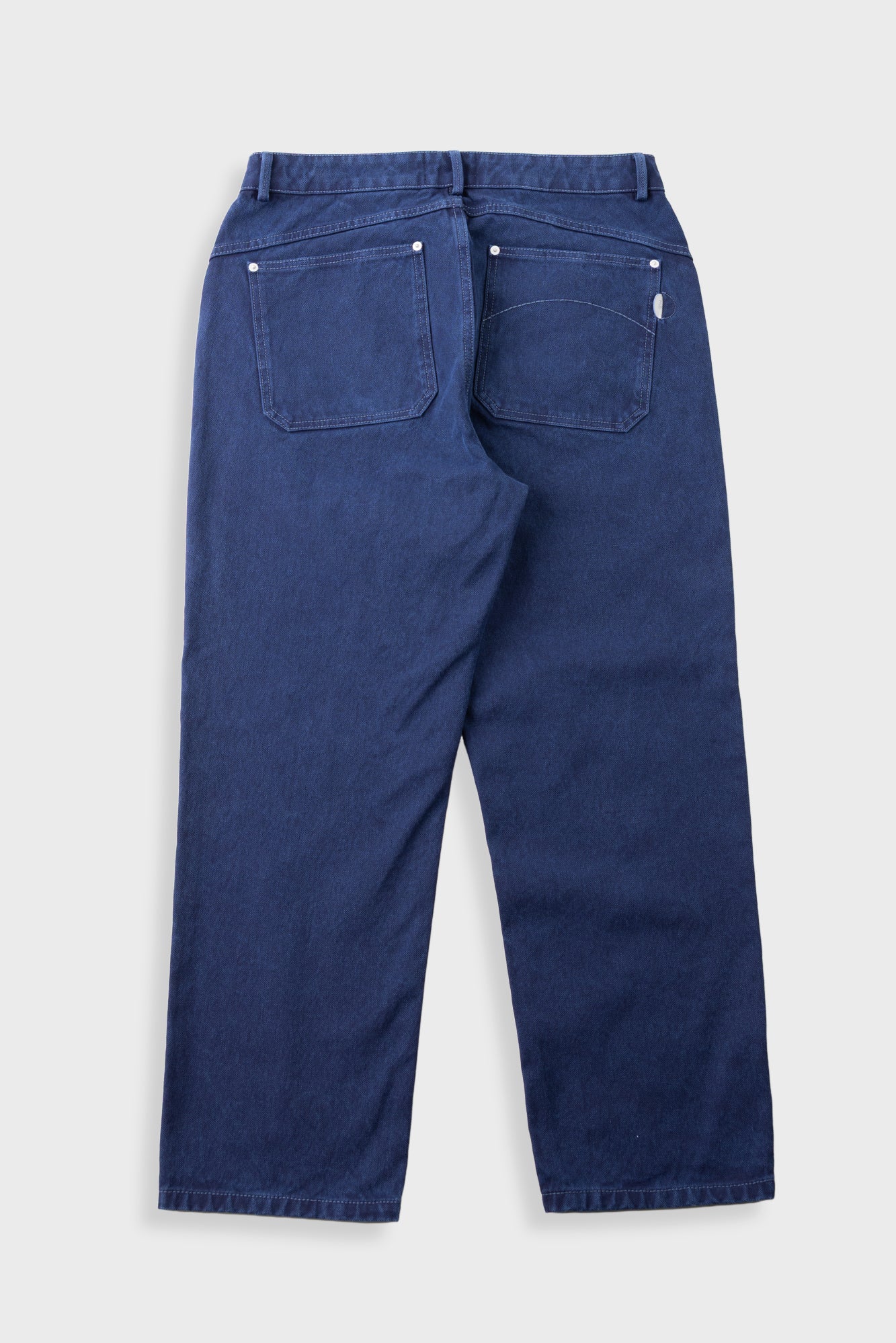 The back view of a pair of dark blue denim jeans, showing the back pockets and button details, photographed flat against a light gray background.