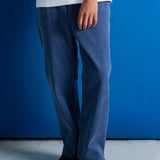 A person wearing loose-fit medium blue denim jeans, a white t-shirt, and black shoes, standing against a solid blue wall.