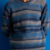 A man wearing a blue and gray striped knit sweater, shown from the neck down against a solid blue background.
