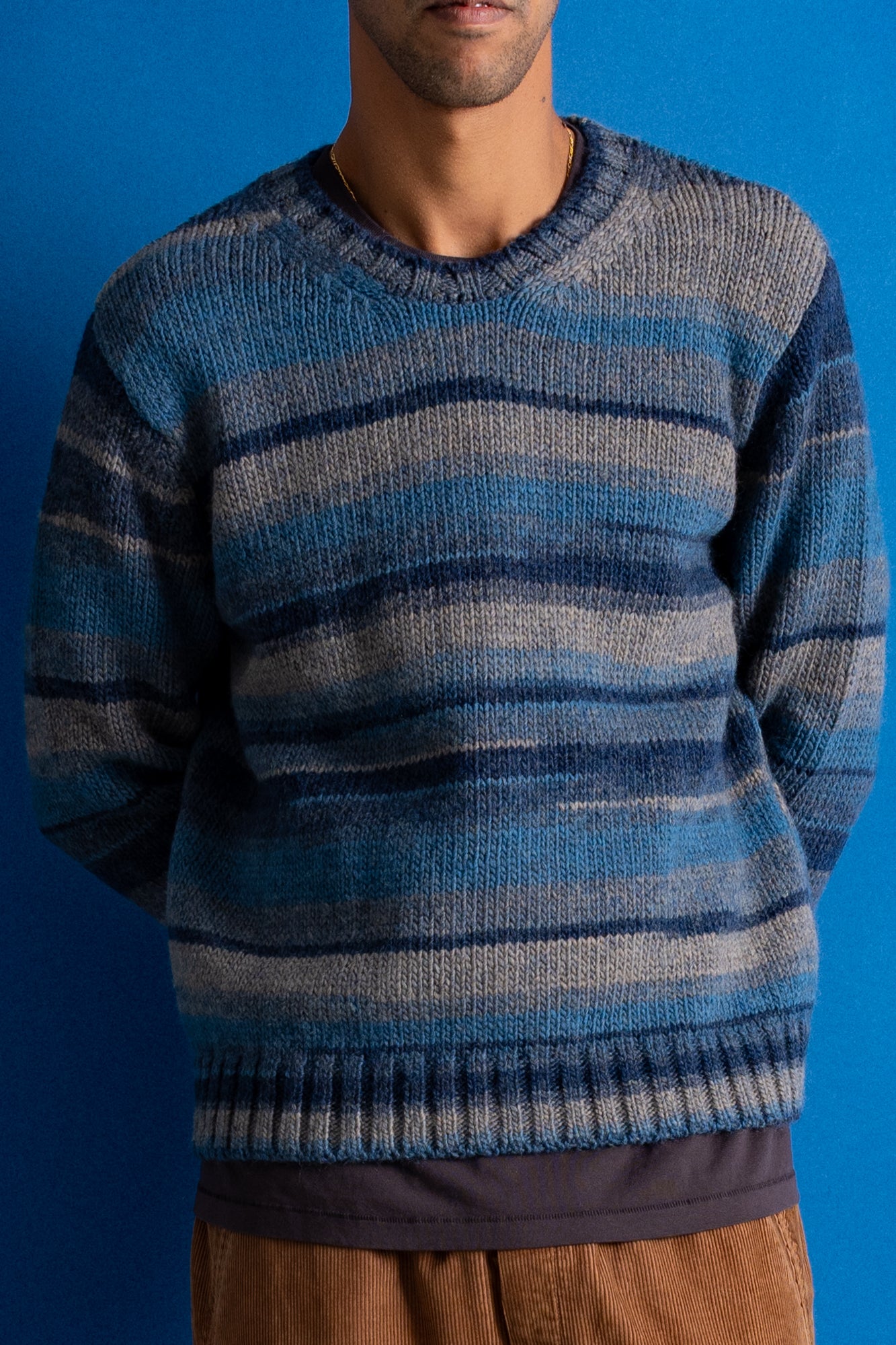 A man wearing a blue and gray striped knit sweater, shown from the neck down against a solid blue background.