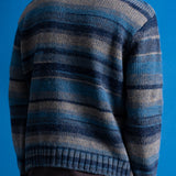 A person shown from the back wearing a blue and gray striped knit sweater, paired with brown pants, against a solid blue background.