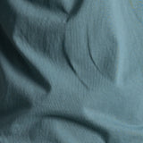 A close-up of draped dusty blue fabric with soft folds and a smooth texture.
