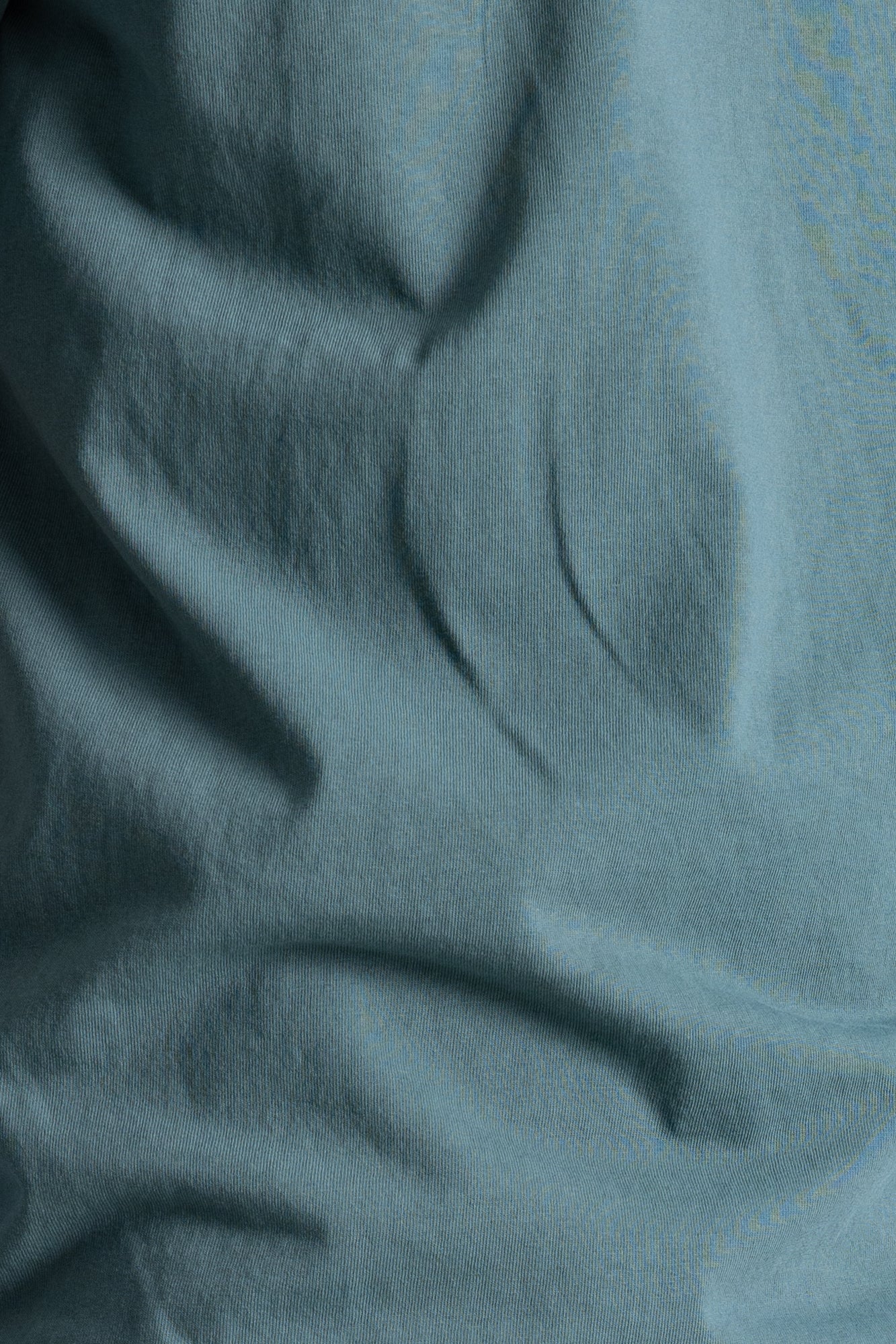 A close-up of draped dusty blue fabric with soft folds and a smooth texture.