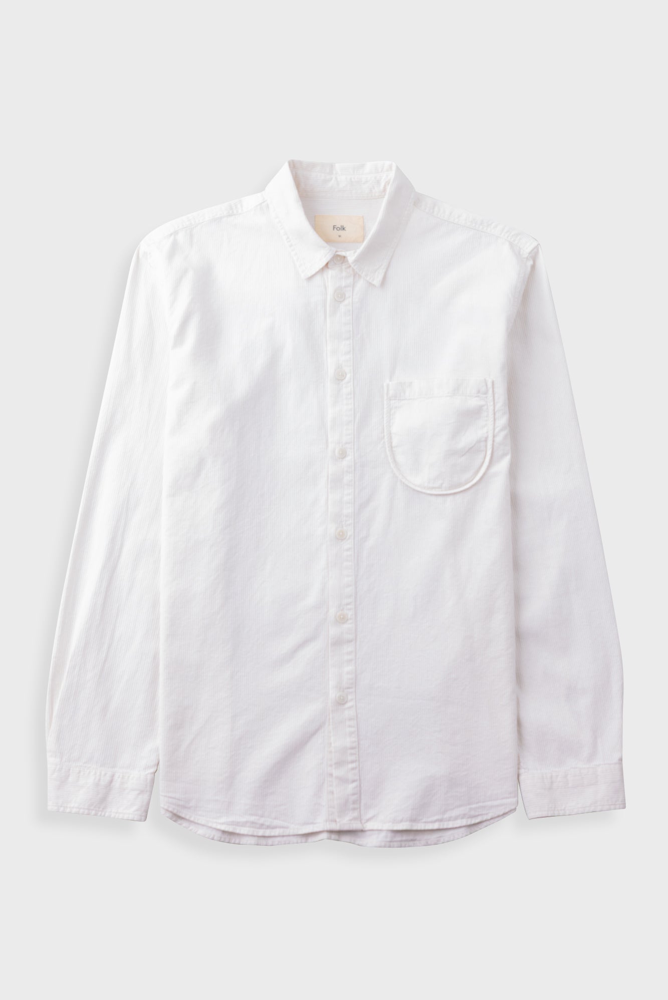 White cotton dress shirt with chest pocket laid flat against a grey background
