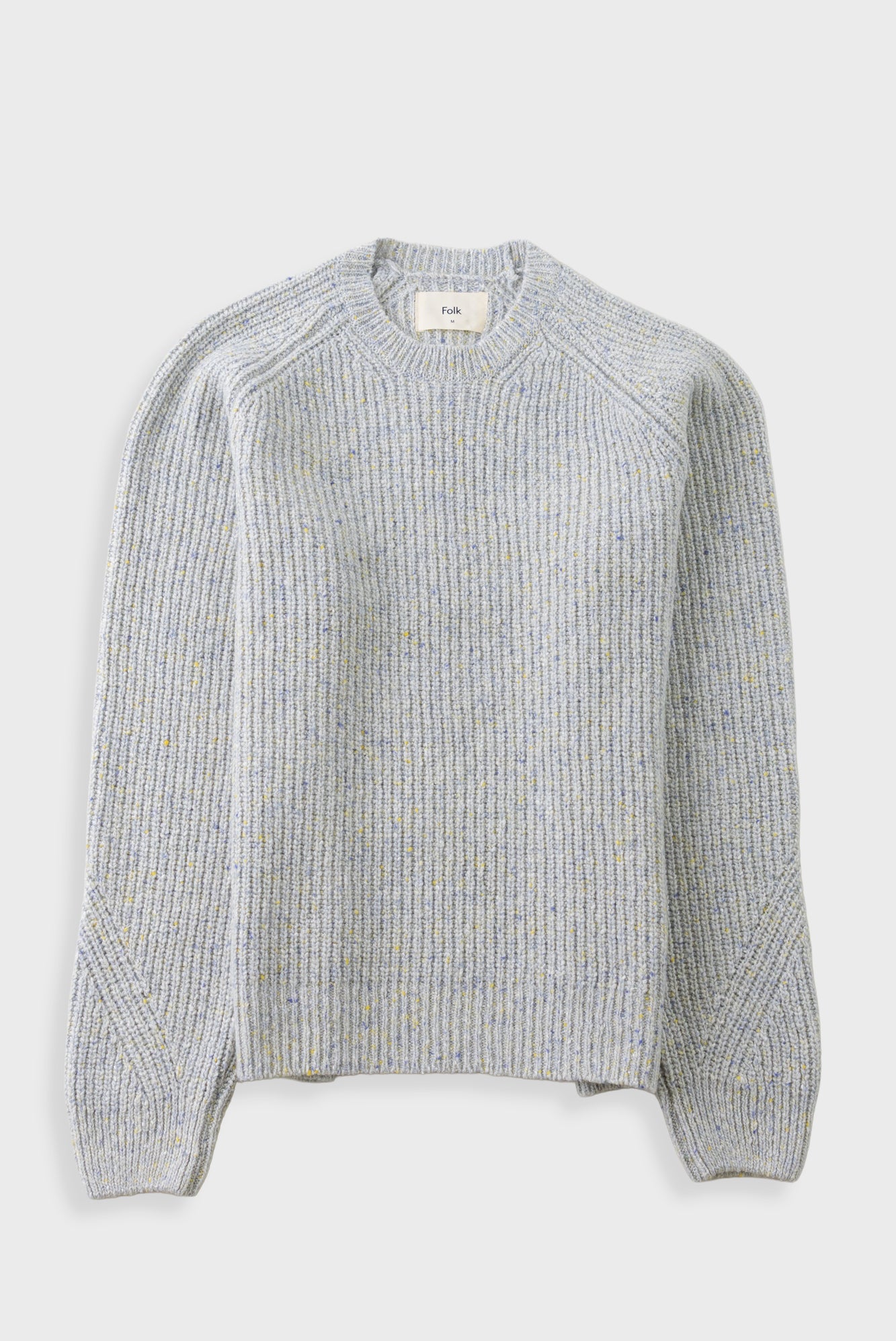 A light gray ribbed knit sweater with subtle yellow and blue flecks throughout, featuring a crew neck and raglan sleeves, shown against a light gray background.