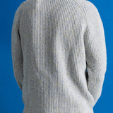 A person shown from the back wearing a light gray ribbed knit sweater over a white shirt, against a solid blue background.