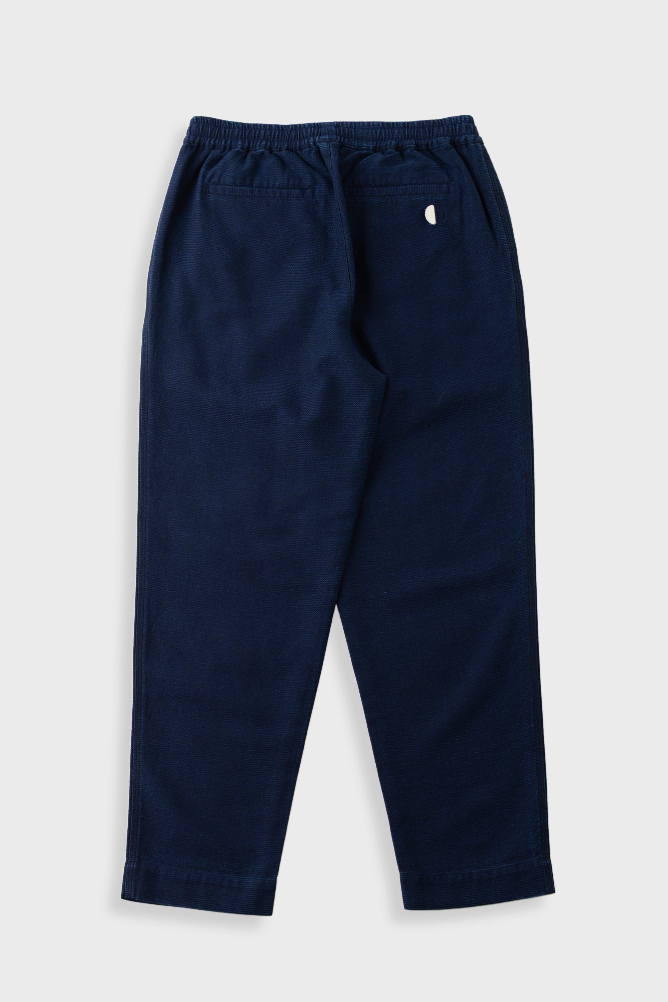 A pair of navy blue pants with an elastic waistband and a small white embroidered logo on the back pocket, shown against a light gray background.