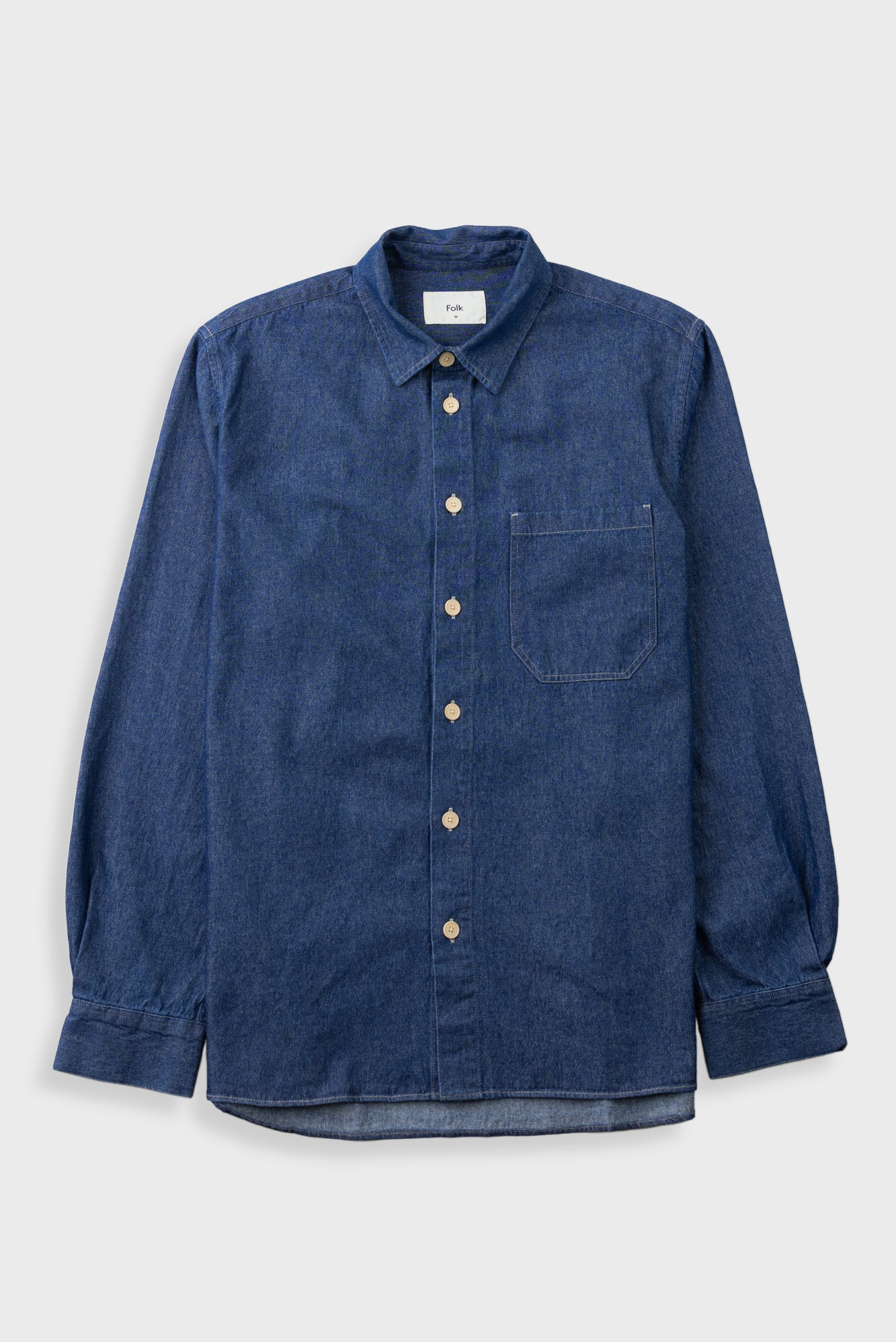 A dark blue denim long-sleeve button-up shirt with a chest pocket, laid flat against a light gray background.