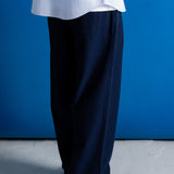 A person shown from the waist down wearing dark navy wide-leg trousers, a light blue shirt, and black shoes, standing against a solid blue wall.